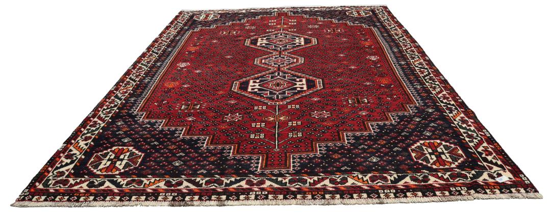 Een handgeknoopt rood Shiraz-tapijt met geometrische patronen en een decoratieve rand.