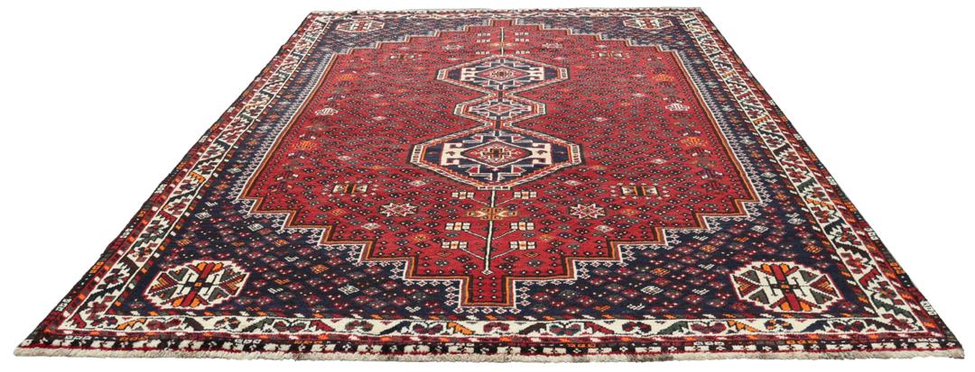 Een handgeknoopt rood Shiraz-tapijt met geometrische patronen en een decoratieve rand.