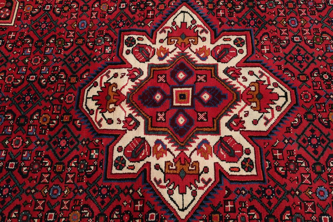 Et håndknyttet Hosseinabad-tæppe fra Mellemøsten med et levende rødt felt og indviklede geometriske mønstre.
