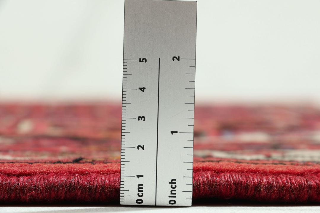 Et håndknyttet Hosseinabad-tæppe fra Mellemøsten med et levende rødt felt og indviklede geometriske mønstre.