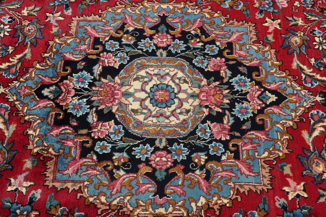 Et håndknyttet Mashad-tæppe fra Mellemøsten med et dybrødt felt og blomstermønstre.