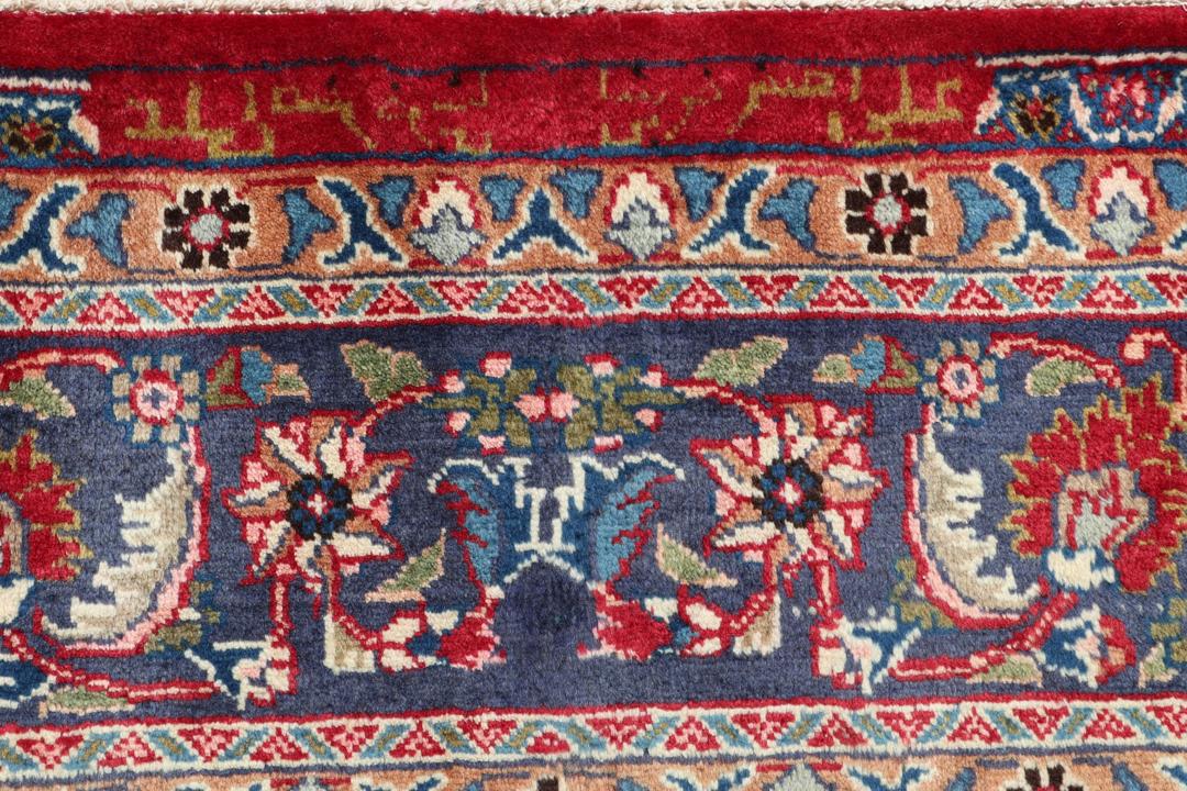 Een groot rechthoekig handgeknoopt Mashad-tapijt uit het Midden-Oosten met een rood veld en blauwe bloempatronen.