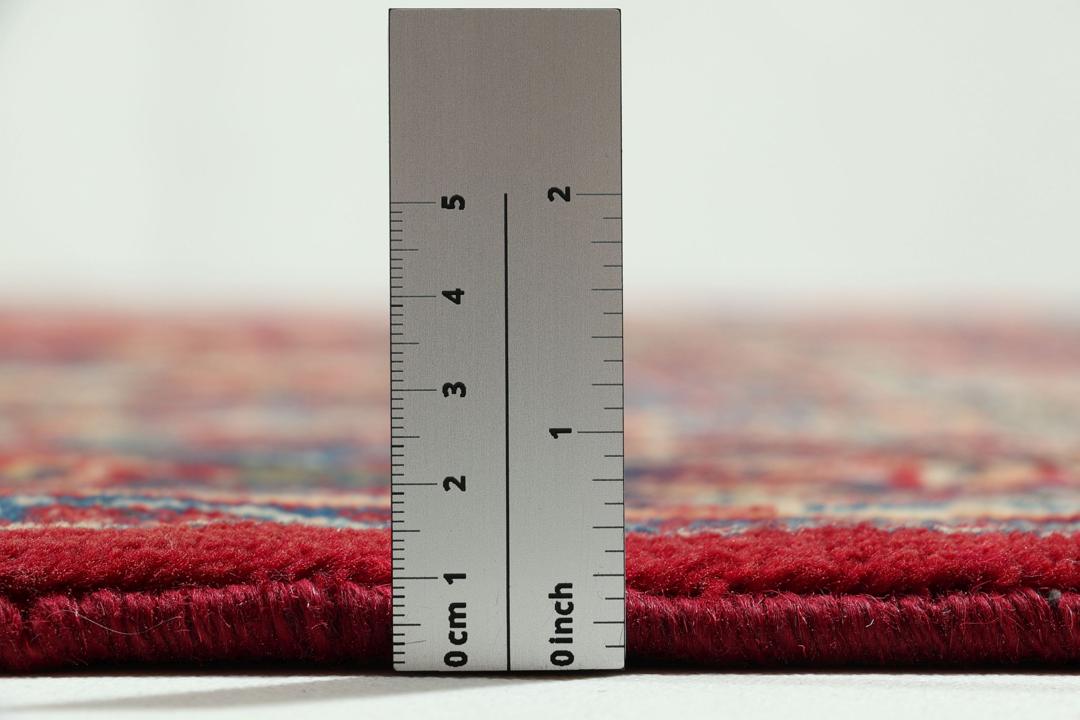 Een groot rechthoekig handgeknoopt Mashad-tapijt uit het Midden-Oosten met een rood veld en blauwe bloempatronen.