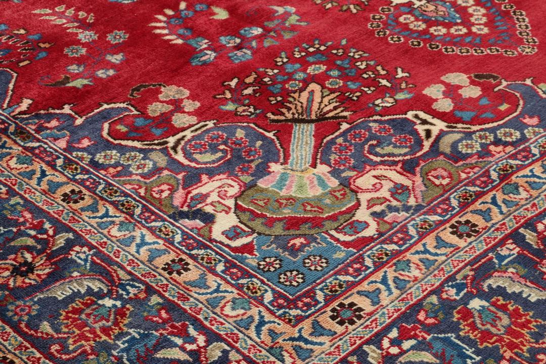 Een groot rechthoekig handgeknoopt Mashad-tapijt uit het Midden-Oosten met een rood veld en blauwe bloempatronen.
