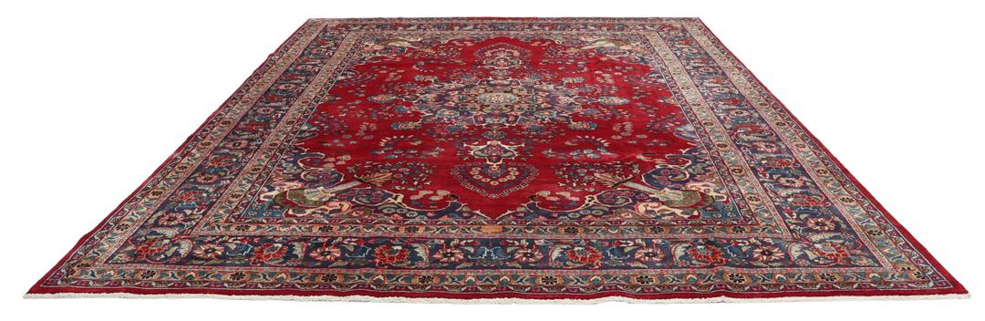 Een groot rechthoekig handgeknoopt Mashad-tapijt uit het Midden-Oosten met een rood veld en blauwe bloempatronen.