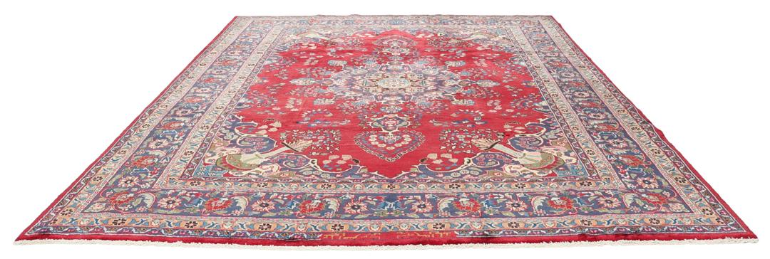 Een groot rechthoekig handgeknoopt Mashad-tapijt uit het Midden-Oosten met een rood veld en blauwe bloempatronen.