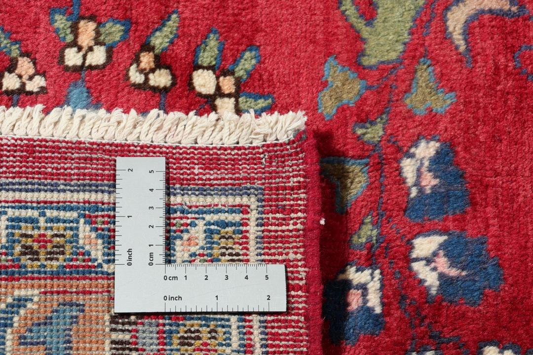 Een groot rechthoekig handgeknoopt Mashad-tapijt uit het Midden-Oosten met een rood veld en blauwe bloempatronen.