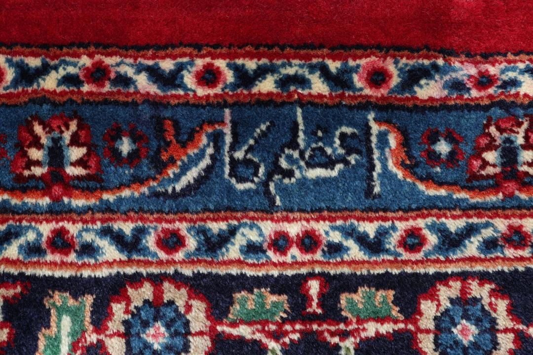 Un tapis Mashad noué main provenant du Moyen-Orient avec un champ rouge profond et des motifs floraux.