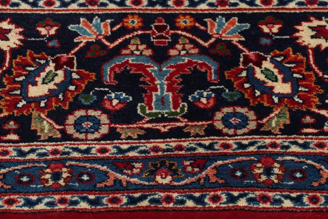 Un tapis Mashad noué main provenant du Moyen-Orient avec un champ rouge profond et des motifs floraux.