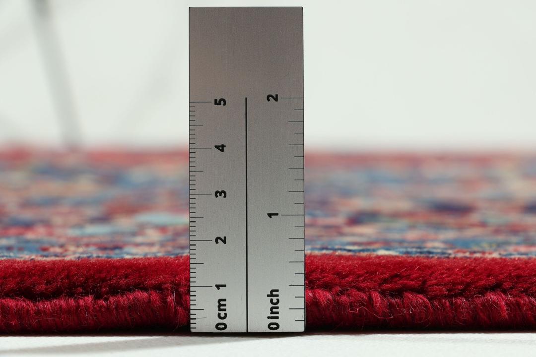 Un tapis Mashad noué main provenant du Moyen-Orient avec un champ rouge profond et des motifs floraux.