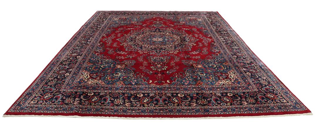 Un tapis Mashad noué main provenant du Moyen-Orient avec un champ rouge profond et des motifs floraux.