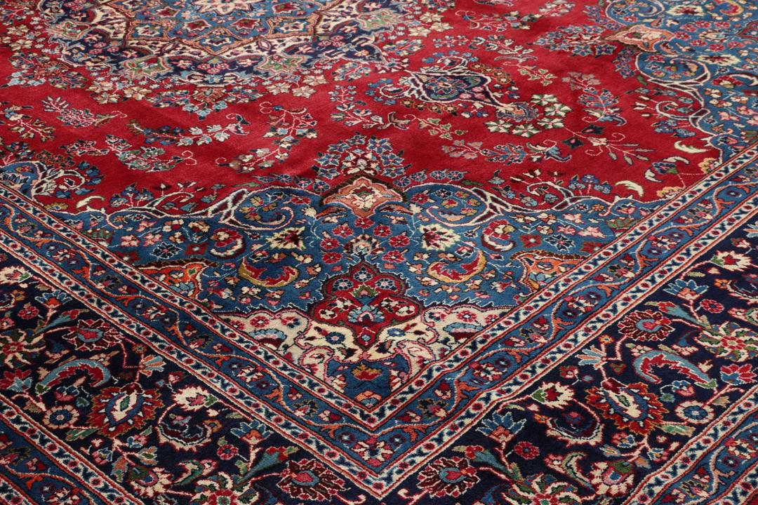 Un tapis Mashad noué main provenant du Moyen-Orient avec un champ rouge profond et des motifs floraux.