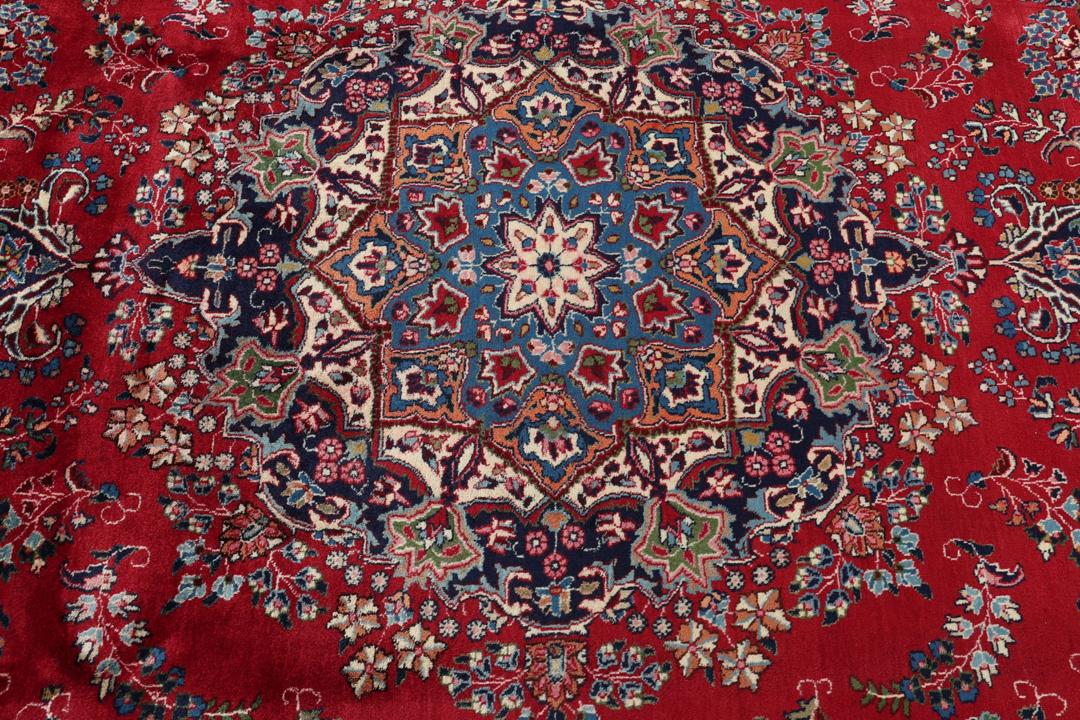 Un tapis Mashad noué main provenant du Moyen-Orient avec un champ rouge profond et des motifs floraux.