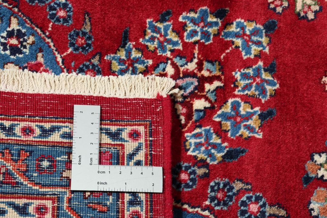 Un tapis Mashad noué main provenant du Moyen-Orient avec un champ rouge profond et des motifs floraux.