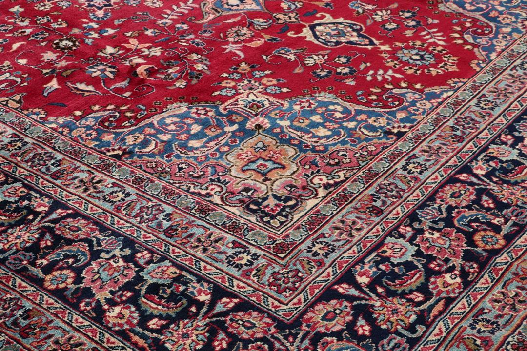 Un tapis Mashad noué main en provenance du Moyen-Orient avec un champ rouge et un motif de médaillon traditionnel.