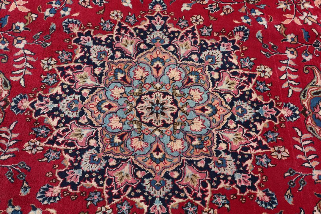 Un tapis Mashad noué main en provenance du Moyen-Orient avec un champ rouge et un motif de médaillon traditionnel.
