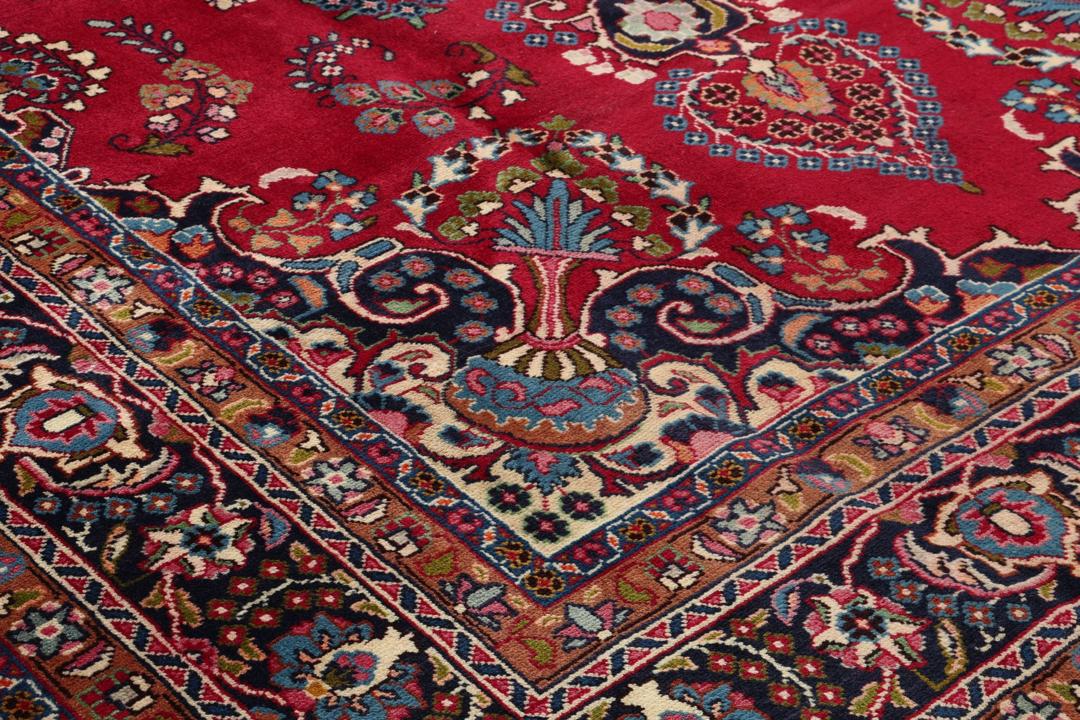 Et håndknyttet Mashad-tæppe fra Mellemøsten med en rød bund og traditionelle blomstermotiver.