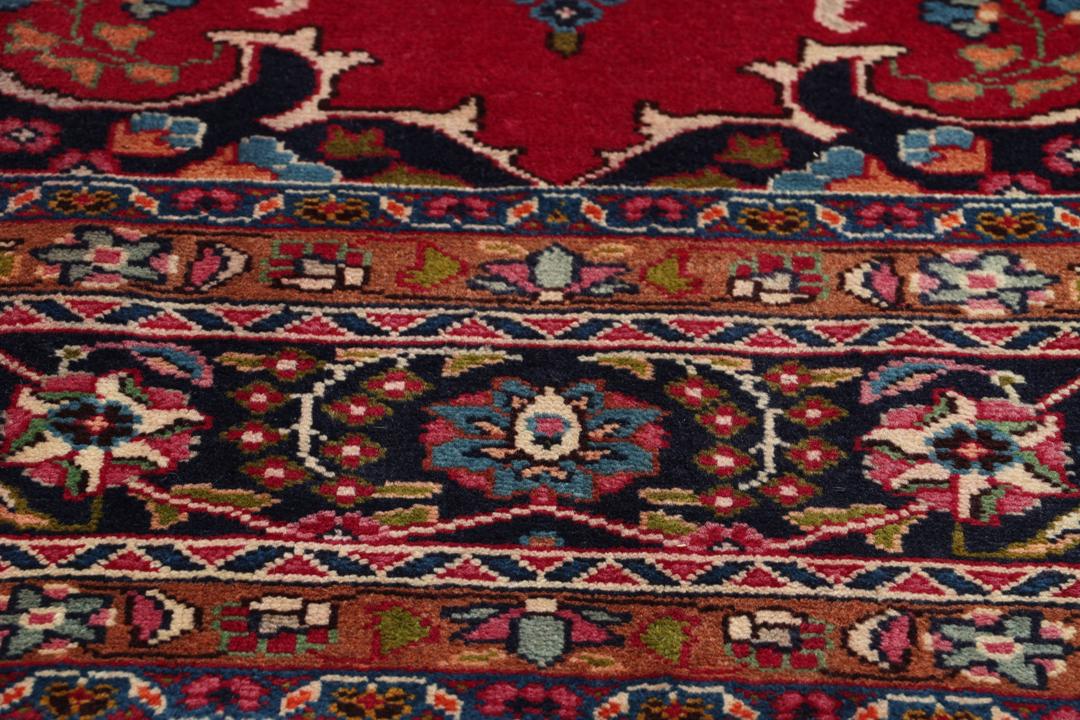 Et håndknyttet Mashad-tæppe fra Mellemøsten med en rød bund og traditionelle blomstermotiver.
