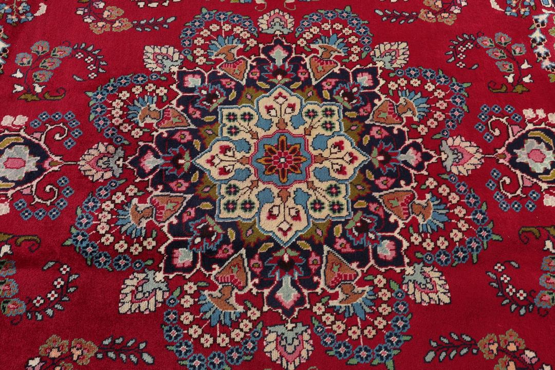Et håndknyttet Mashad-tæppe fra Mellemøsten med en rød bund og traditionelle blomstermotiver.