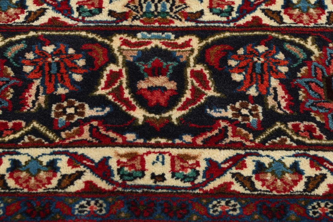 A hand-knotted Mashad rug from the Middle East in deep red and navy tones.