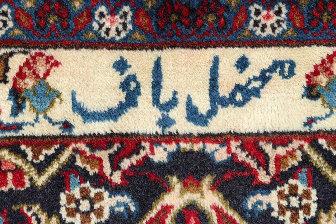 A hand-knotted Mashad rug from the Middle East in deep red and navy tones.