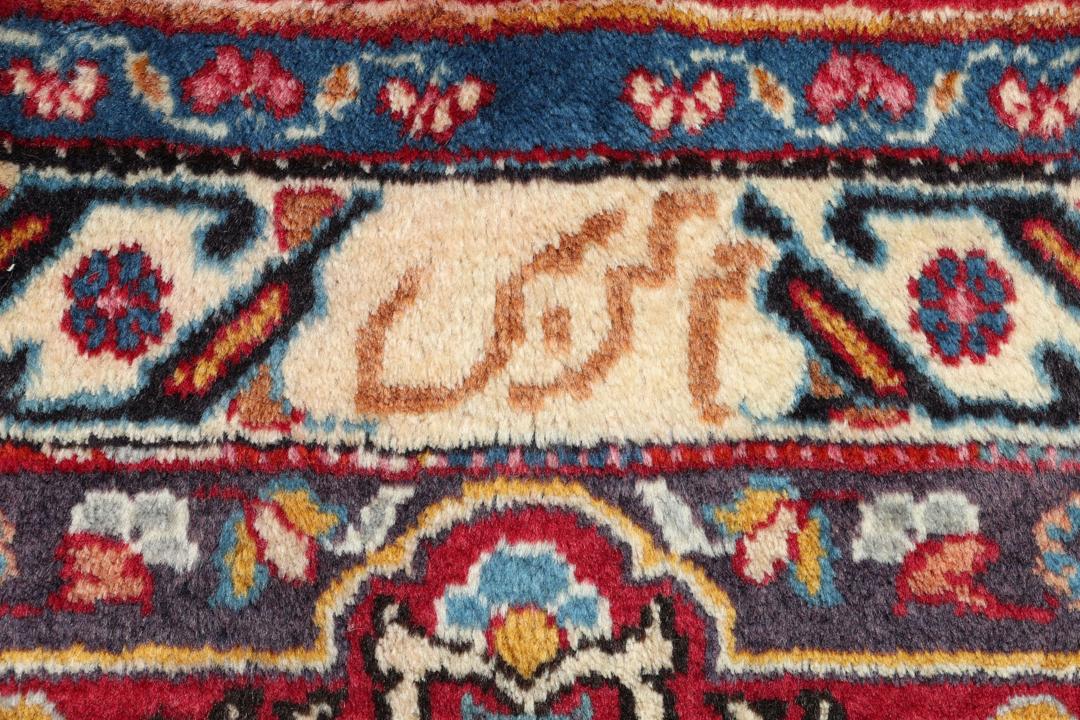 A large rectangular Mashad rug from the Middle East in deep red with floral medallion patterns.