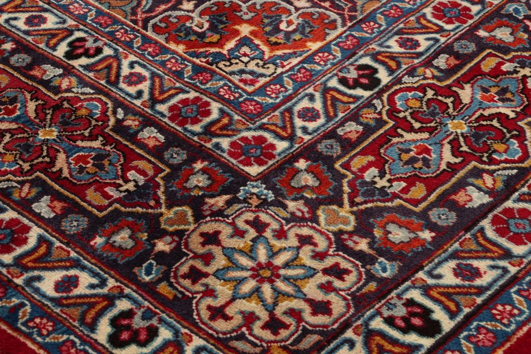 A large rectangular Mashad rug from the Middle East in deep red with floral medallion patterns.