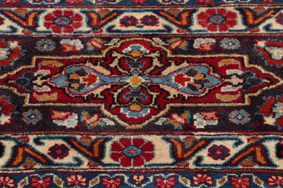 A large rectangular Mashad rug from the Middle East in deep red with floral medallion patterns.