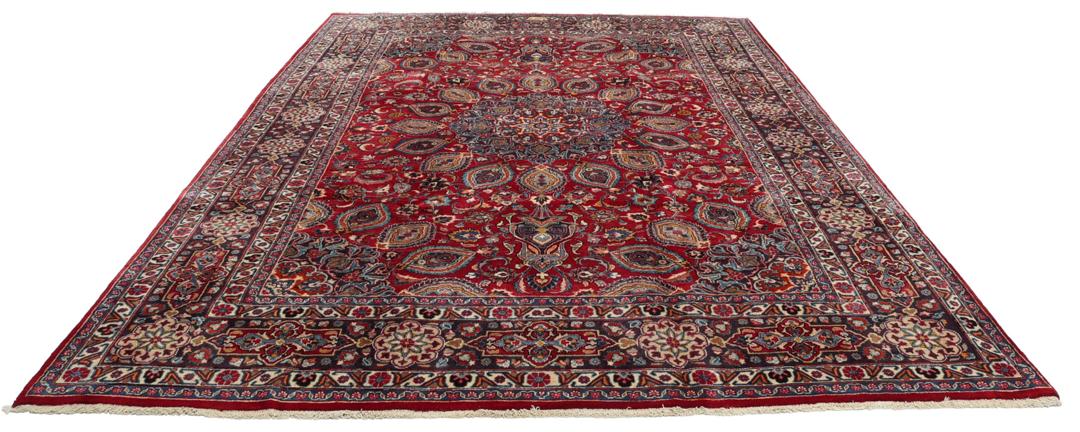 A large rectangular Mashad rug from the Middle East in deep red with floral medallion patterns.
