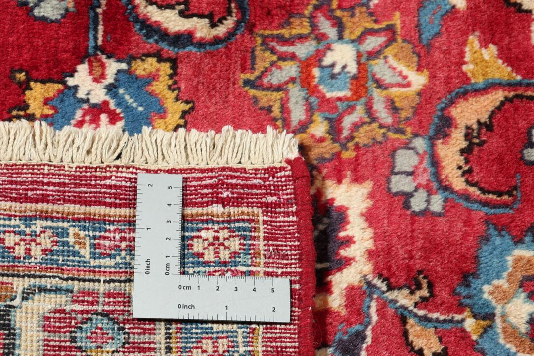 A large rectangular Mashad rug from the Middle East in deep red with floral medallion patterns.