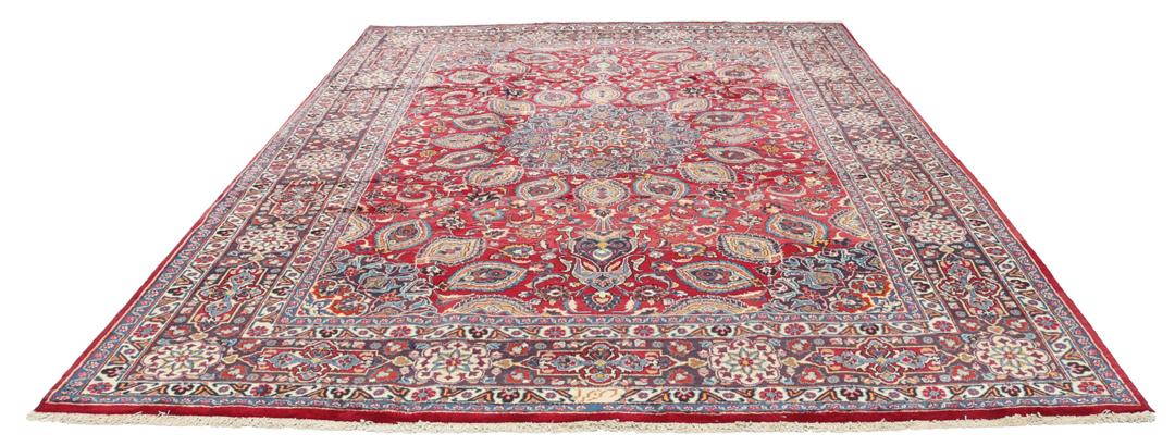 A large rectangular Mashad rug from the Middle East in deep red with floral medallion patterns.