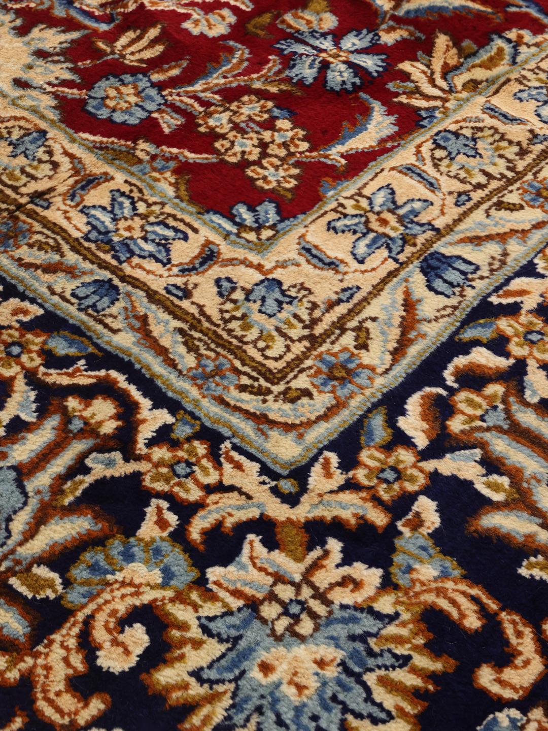 A hand-knotted Kerman rug from the Middle East featuring a vibrant red field and intricate floral patterns.