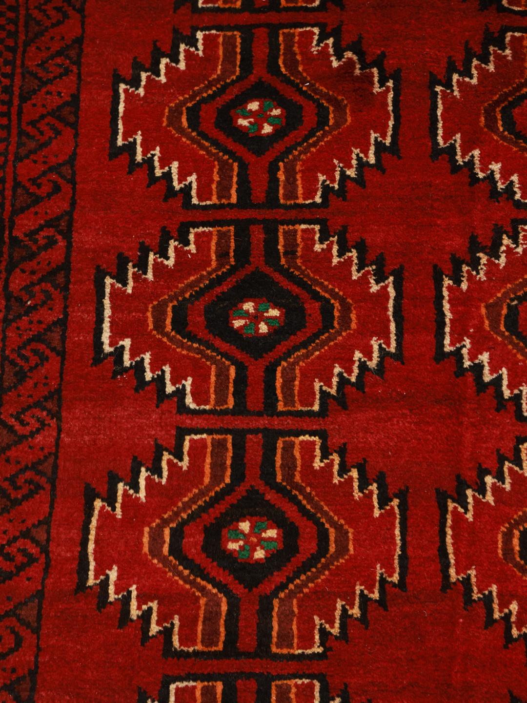 Een handgeknoopt Beluch-tapijt uit het Midden-Oosten in donkerrood met geometrische patronen.