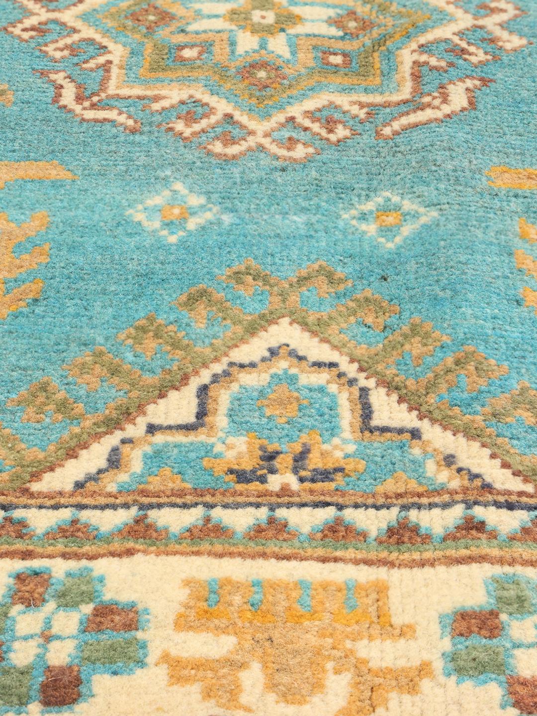 Et håndknyttet afghansk Kazak-tæppe med et levende blågrønt felt og geometriske mønstre.