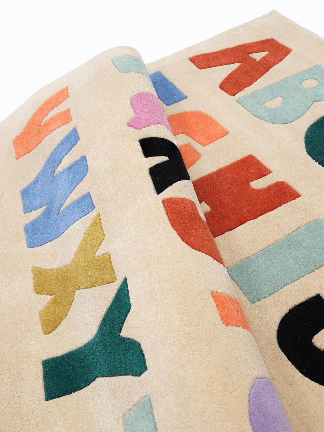 Et beige tæppe med et farverigt alfabetmønster i forskellige nuancer