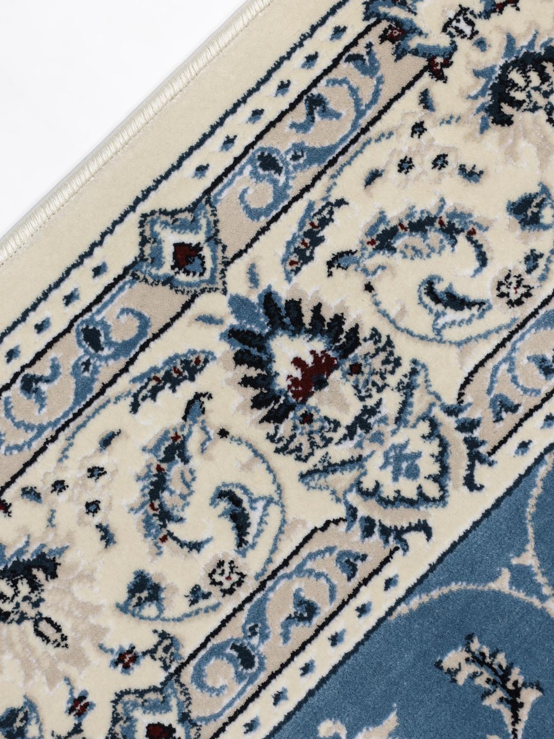 Lyseblåt tæppe med traditionelle blomstermotiver og dekorative kanter