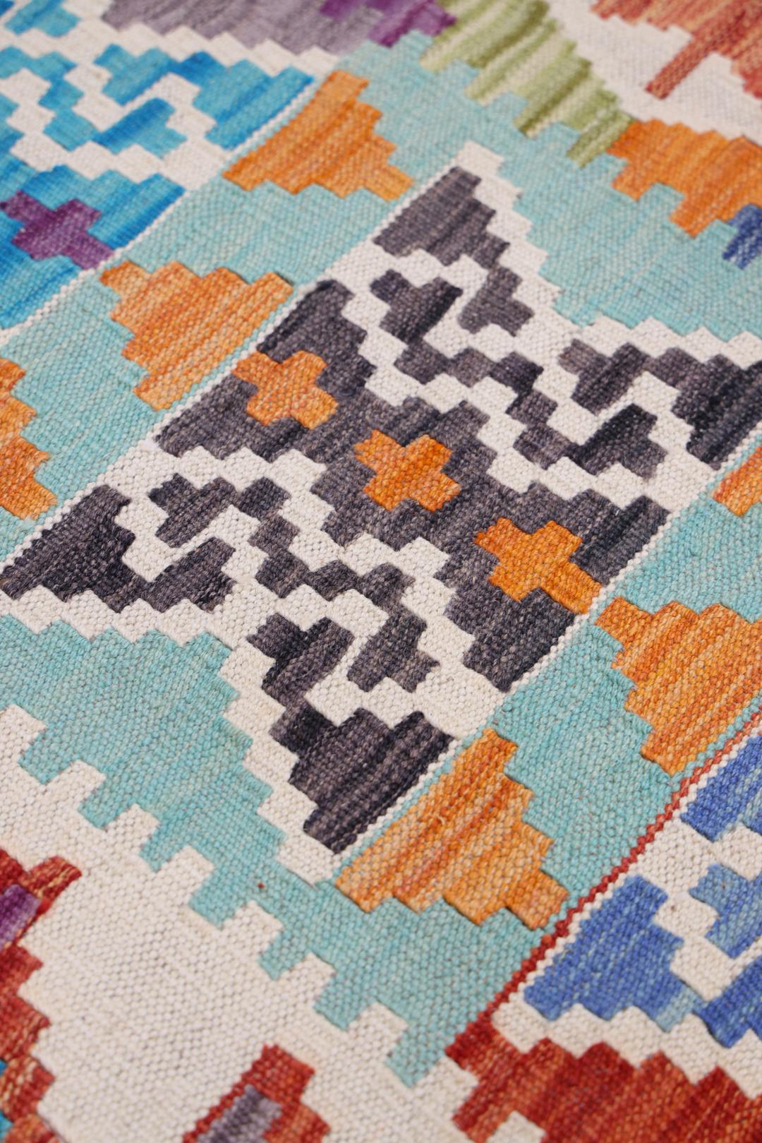 A large, colourful hand-woven Afghan Kelim rug with geometric diamond patterns.