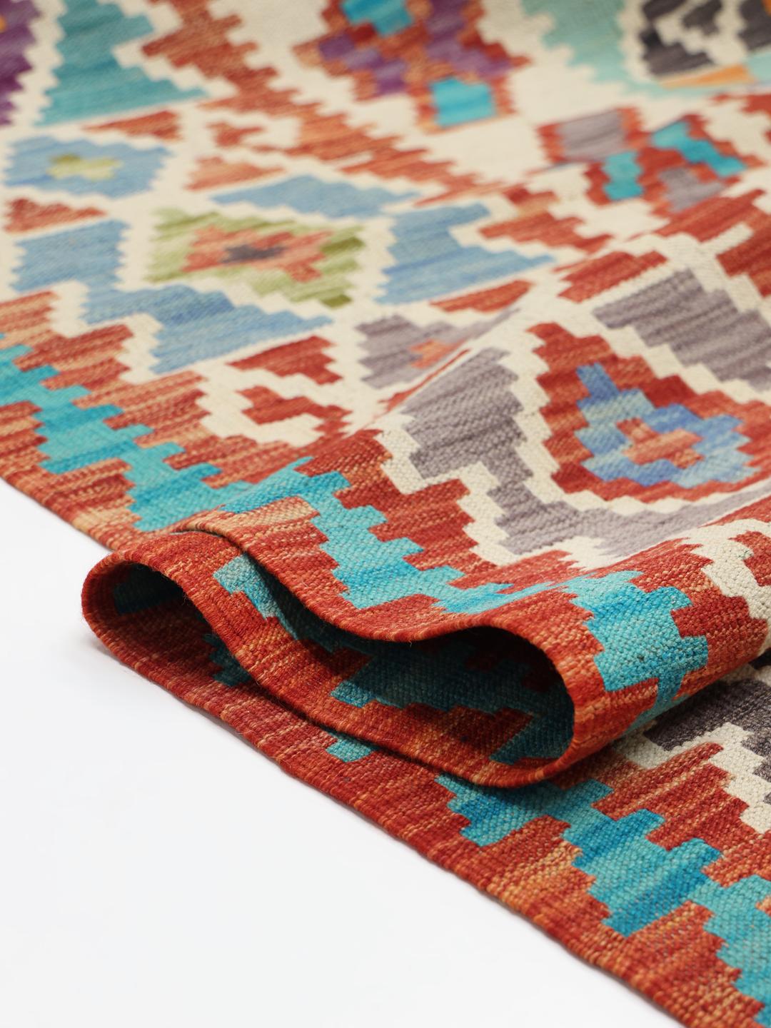 A large, colourful hand-woven Afghan Kelim rug with geometric diamond patterns.