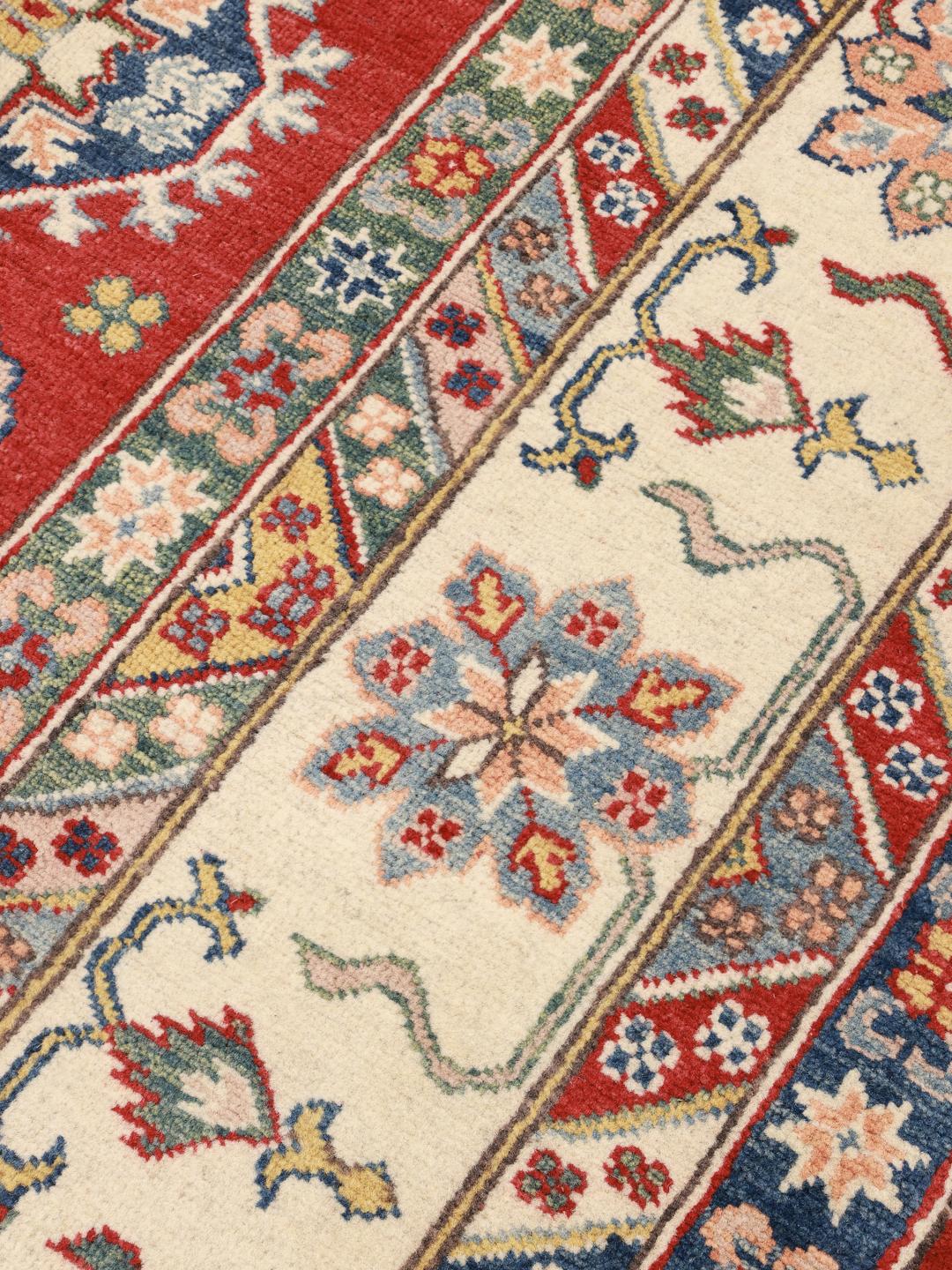 Un covor Kazak înnodat manual din Afganistan, prezentând un câmp roșu și medalioane geometrice colorate.