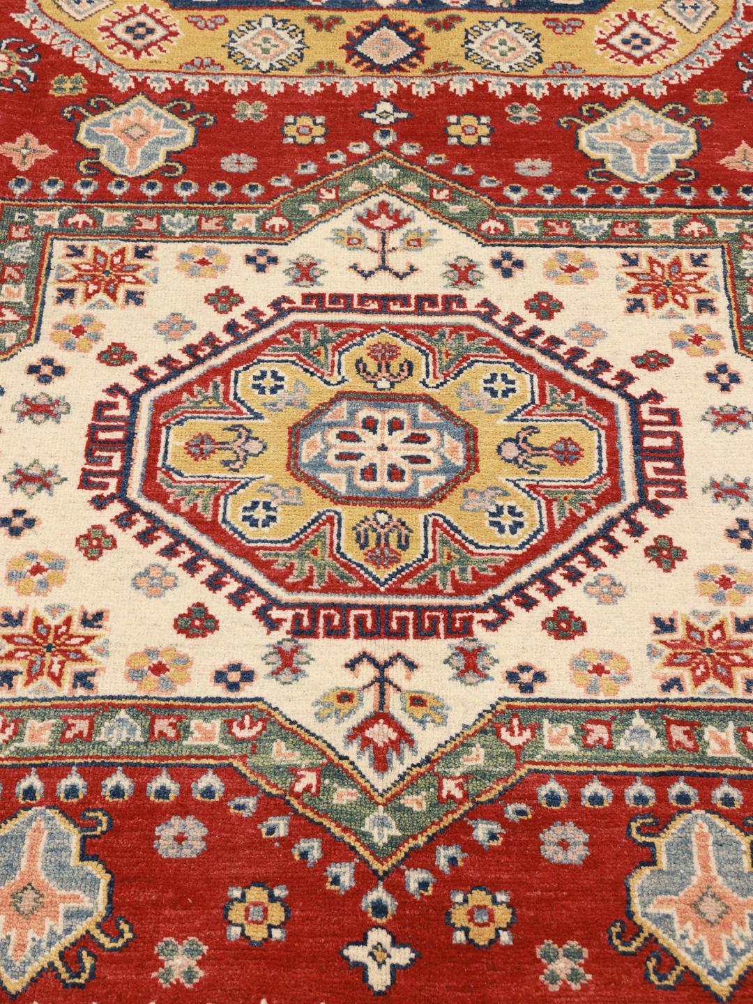 Un covor Kazak înnodat manual din Afganistan, prezentând un câmp roșu și medalioane geometrice colorate.