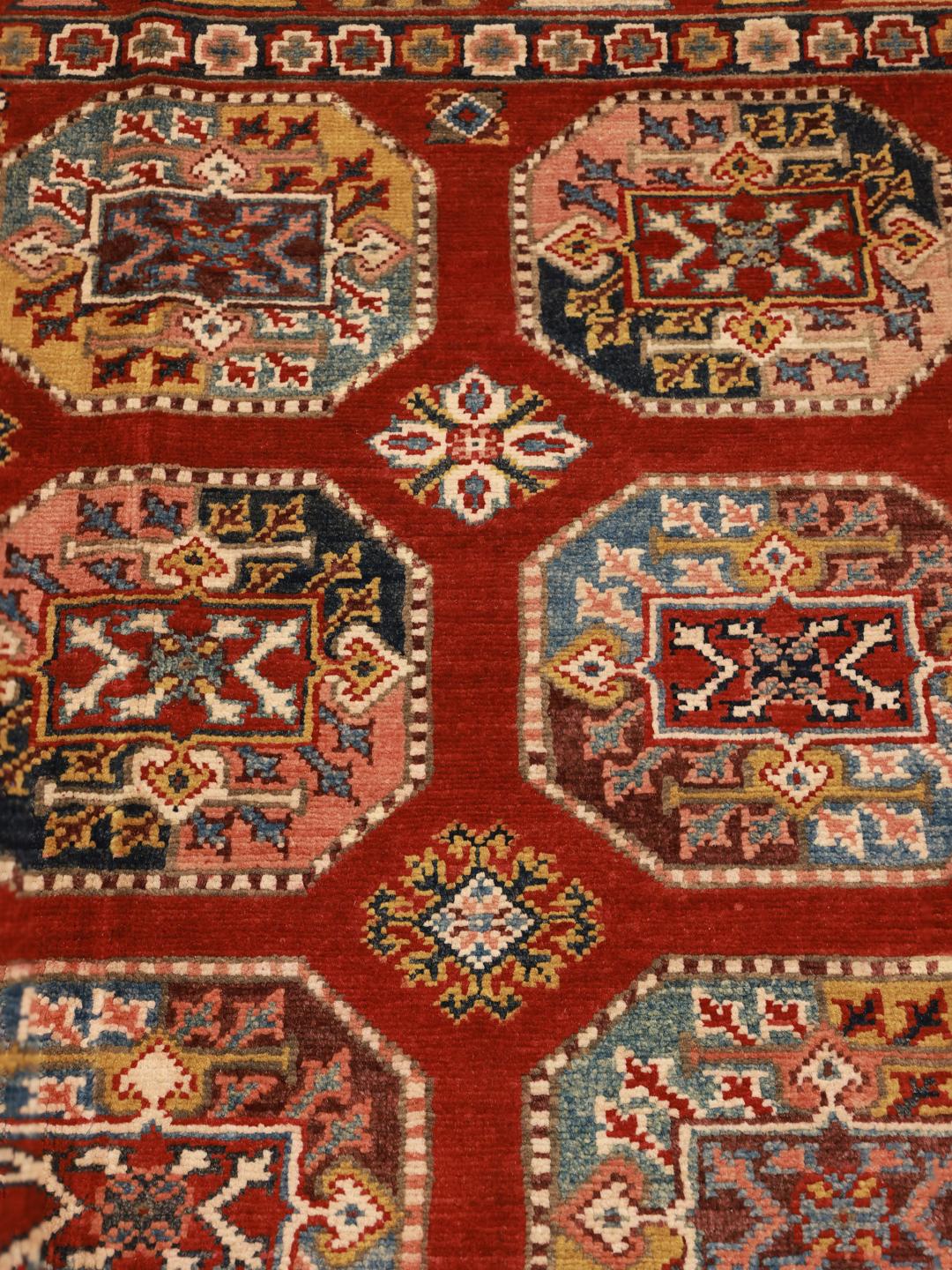 A hand-knotted Kazak rug from Afghanistan with a vibrant red field and geometric patterns.