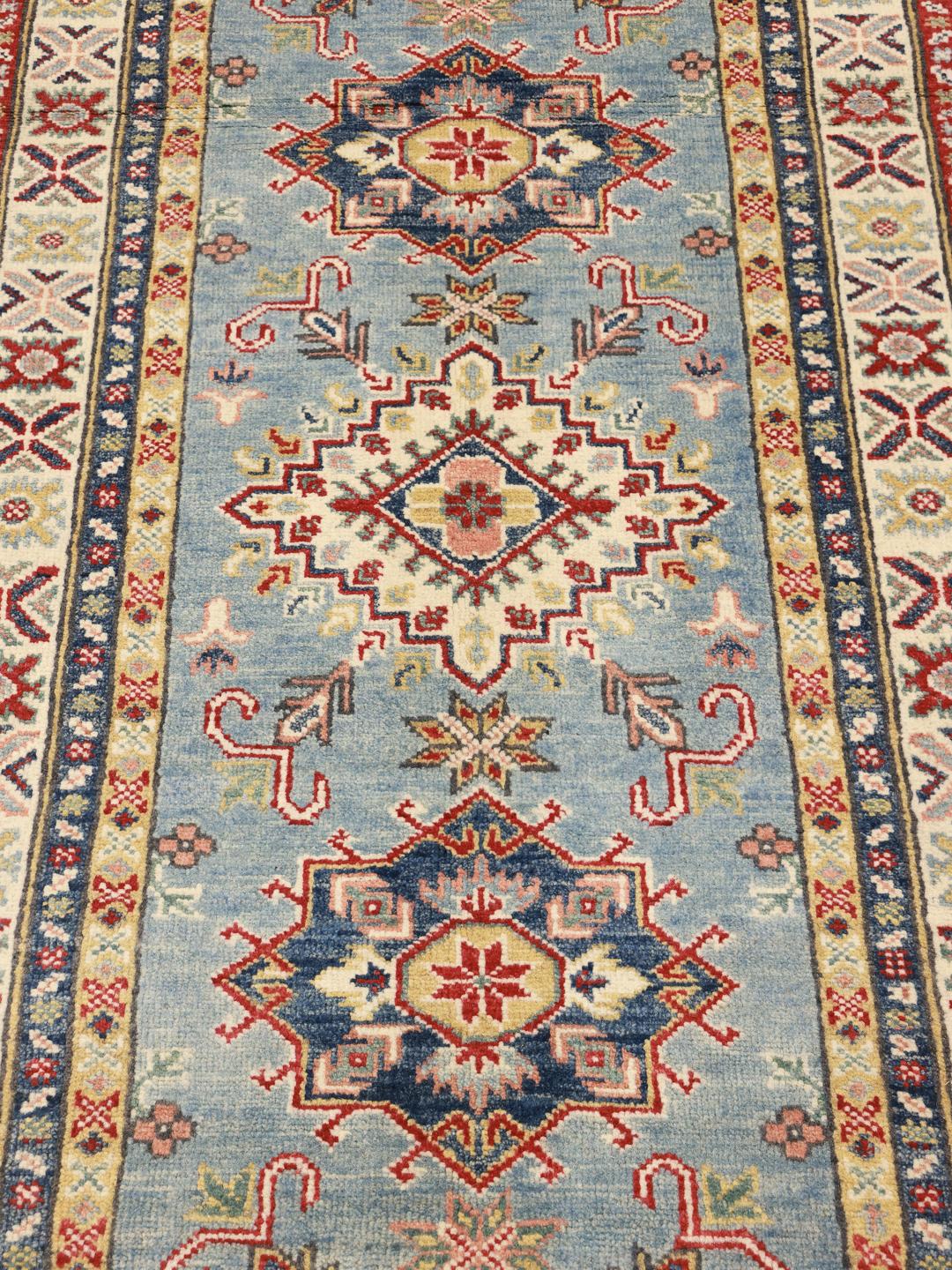 Un tapis couloir Kazak noué à la main en provenance d'Afghanistan présentant des motifs géométriques en bleu, rouge et crème.