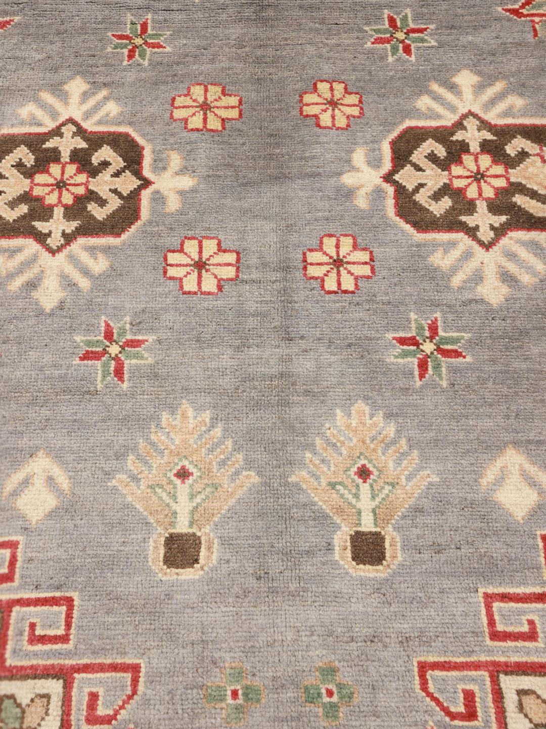 Een groot, handgeknoopt Kazak-tapijt uit Afghanistan in grijstinten en rood.