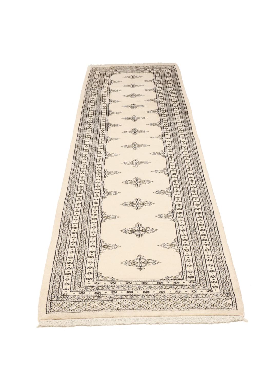 A long, beige hand-knotted runner from Pakistan with black repeating motifs.