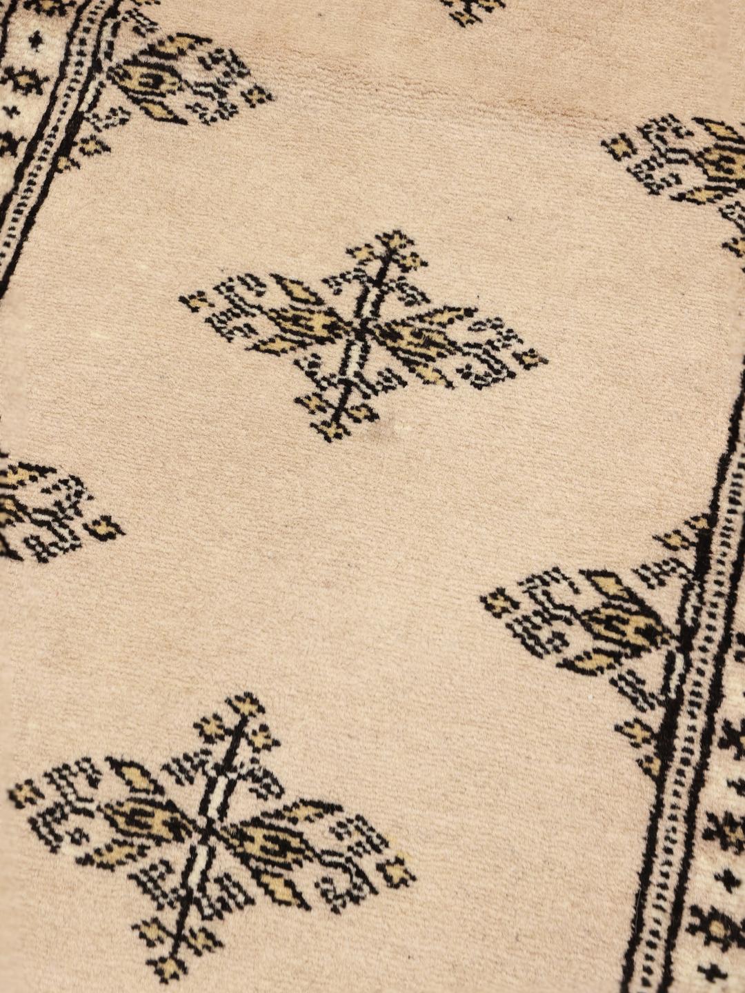 A long, beige hand-knotted runner from Pakistan with black repeating motifs.