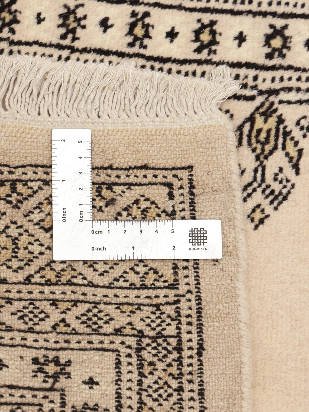 A long, beige hand-knotted runner from Pakistan with black repeating motifs.