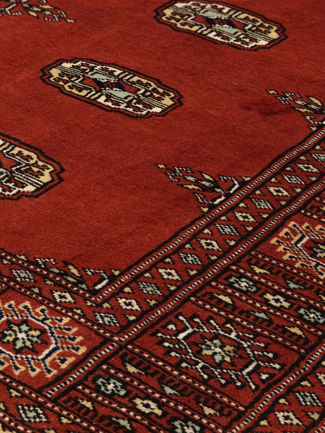 Hand-knotted Pakistan Bokhara rug with a vibrant red field and traditional geometric motifs