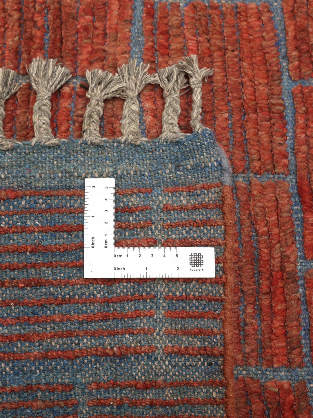 Et håndknyttet uldtæppe fra Afghanistan med et rødt murstenslignende mønster og blå detaljer.