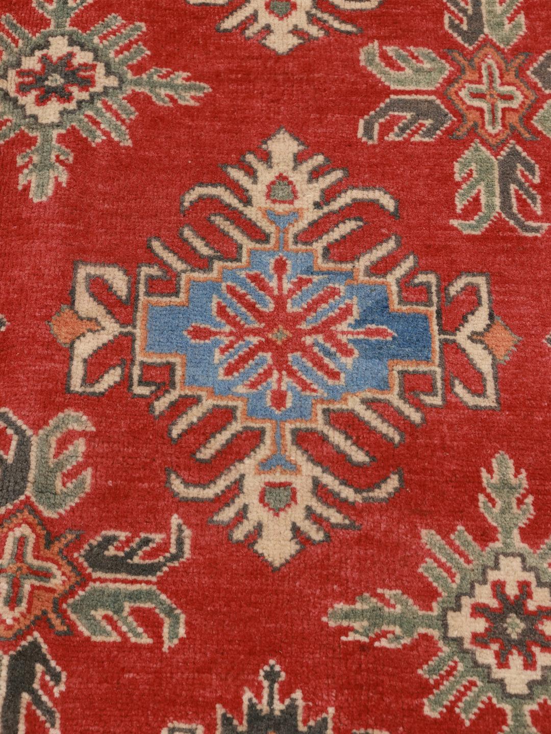 Duży prostokątny afgański dywan Kazak z żywym czerwonym tłem oraz niebieskimi i beżowymi geometrycznymi motywami.