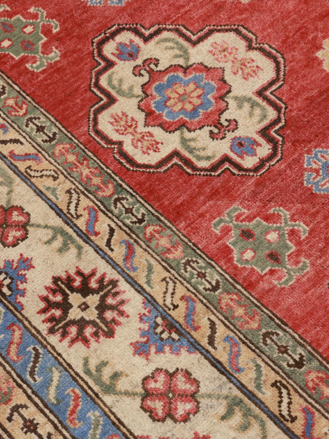 Ein handgeknüpfter afghanischer Kazak-Teppich mit einem lebendigen roten Feld und komplexen geometrischen Mustern.